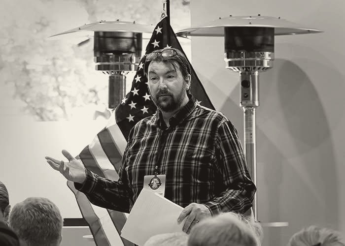 Bjorn Handeen addressing a meeting in front of an American flag